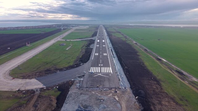 Aerial view straight down an airport runway disappearing into dense fog, with fresh runway markings, threshold stripes and surrounding construction areas creating a dramatic low-visibility aviation sc