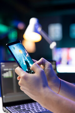 Selective focus of a person holding a cell phone and playing video games. Closeup of an individual entertaining oneself with a space shooter game on a mobile device.