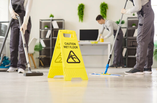 Cleaners janitors team mopping office with caution cleaning. Wet floor signage, vacuuming and mop indicate hygiene standards and slip prevention. Workplace cleaning and safety concept image.