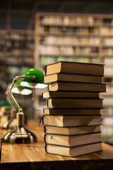 Close up of stacked books on desk in quiet university library with warm lighting and green lamp, educational environment with bookshelves and study materials, empty library study space. © DC Studio