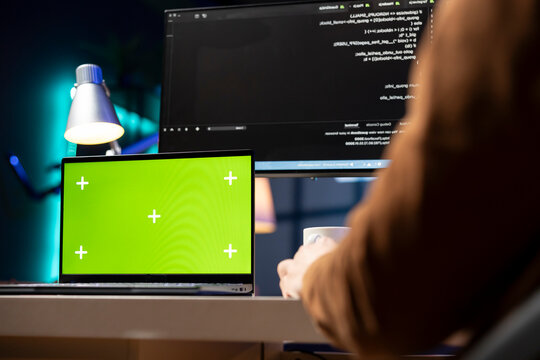 Man working from home using isolated screen laptop, testing and deploying programs and systems. Programmer checking code displayed on computer monitors using chroma key notebook.