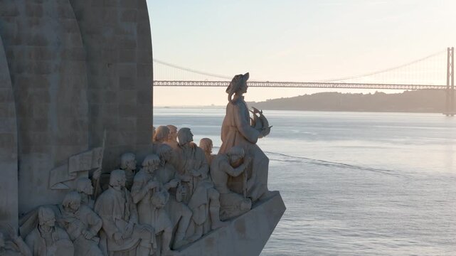 Aerial view of the Monument to the Discoveries with the 25 de Abril Bridge over the Tagus River during golden hour in Lisboa, Lisboa, Portugal.
