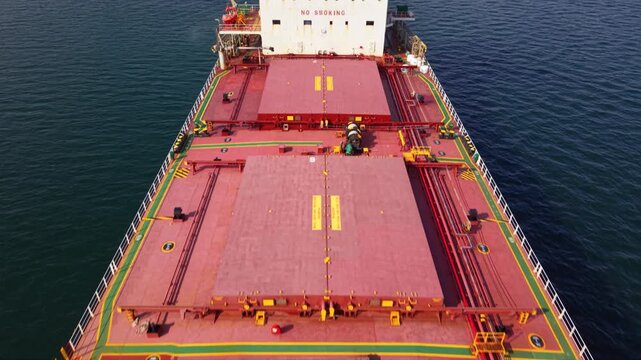 Aerial view from above a cargo ship&rsquo;s deck with large hatch covers and a helipad marking, sailing on open water