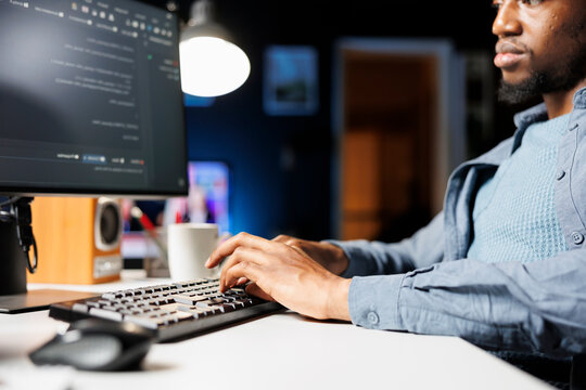 Network administrator functioning via computer programming at home, entering script code for safety and confidentiality; on terminal window, african american technician diagnoses system.