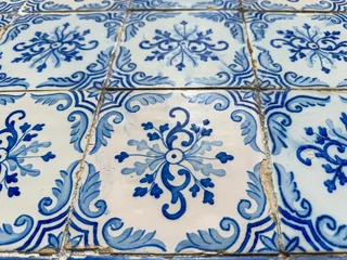 Close-up of weathered Portuguese azulejo tiles with intricate blue floral scrollwork patterns set against a crisp white glazed ceramic background © anammarques