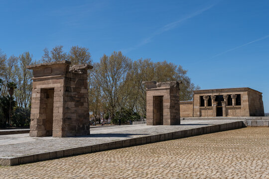 A horizontal eye-level shot of the historic Temple of Debod, an ancient Egyptian temple rebuilt in a public park in Madrid, Spain, under a clear blue sky.