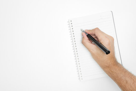 Top view of a male hand writing with a black fountain pen in a blank spiral notebook isolated on a white background with copy space