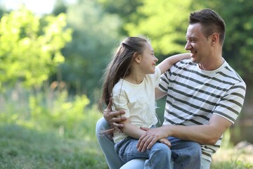 Fototapeta premium Smiling father and his daughter looking at each other outdoors on sunny day. Space for text