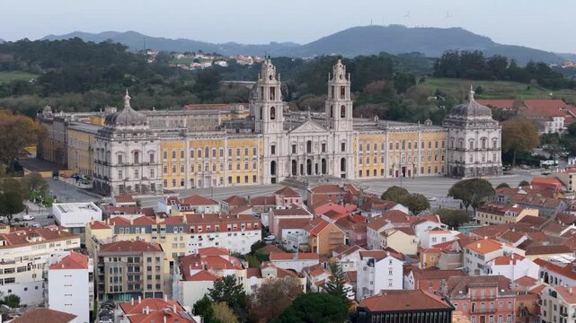 Aerial view of the historic Mafra National Palace with its baroque facade and bell towers overlooking the red-roofed houses of the town Mafra, Lisbon, Portugal.