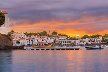 Fototapeta premium Traditional boat moored in the harbor of Cadaques during sunrise with colorful clouds reflecting on calm water.
