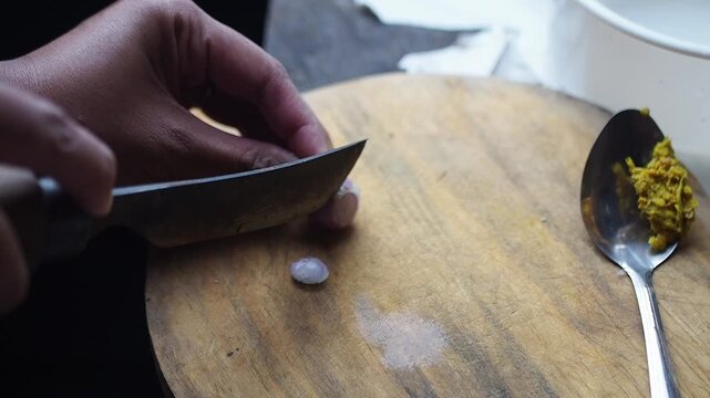 Close-up of a person's hands finely dicing a shallot on a wooden cutting board for cooking preparation in a kitchen.