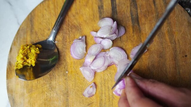 Close-up of hands chopping shallots on a wooden cutting board with a spoon of ginger paste