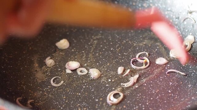 Chopped shallots being sauteed in a non-stick pan with oil, stirred with a red silicone spatula, cooking and preparation process