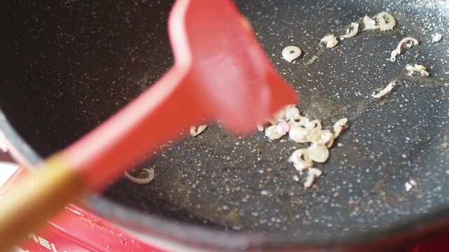 Frying chopped shallots and curry paste in a non-stick pan with a red silicone spatula and spoon