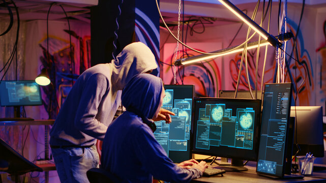 Hackers in neon lit room writing lines of code on computer, having burst of joy after successfully get past security systems with their virus, scammers happy after finishing working hacking script.