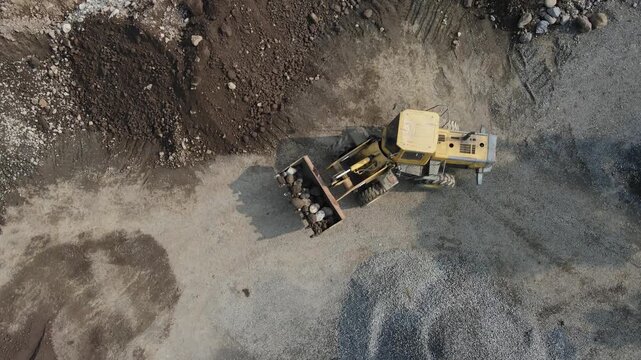 Aerial view of a yellow wheel loader moving heavy rocks and gravel at a construction site in Pegalongan, Patikraja, Central Java, Indonesia.