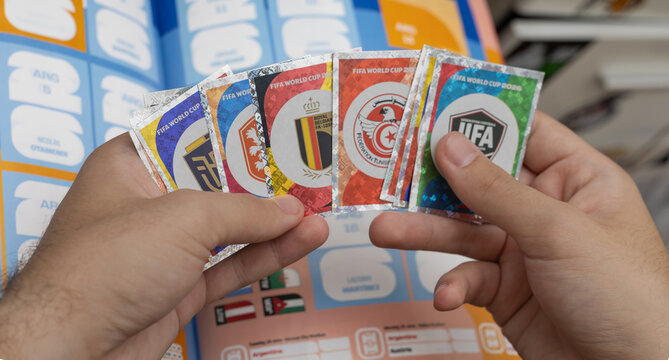 top-down, close-up shot of hands holding a fan of shiny 2026 FIFA World Cup sticker collection badges over an open sticker album page