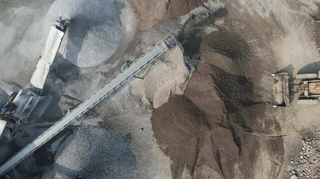 Aerial view of a yellow wheel loader moving piles of earth and gravel at the Pegalongan construction site in Patikraja, Central Java, Indonesia.