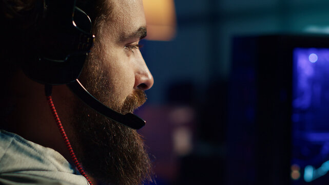 Pro gamer at home talking with teammates, competing together in intense online multiplayer video game, extreme close-up, man having gaming session with friends, using powerful computer to play game.