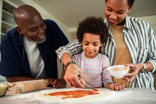 Parents helping child make pizza in home kitchen