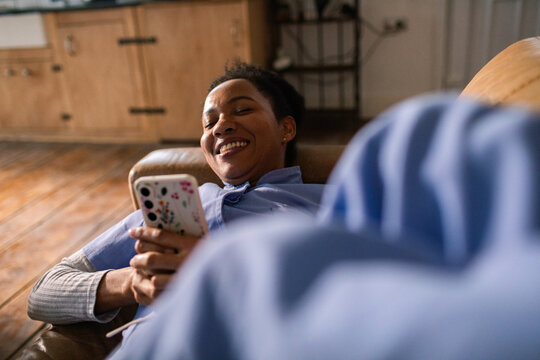 Smiling woman relaxing on sofa using smartphone at home