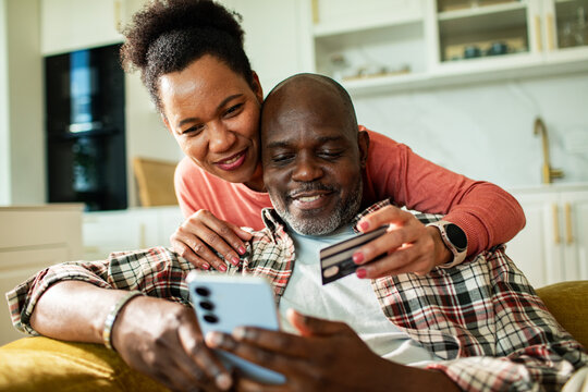 Happy couple paying with smartphone and credit card in home kitchen