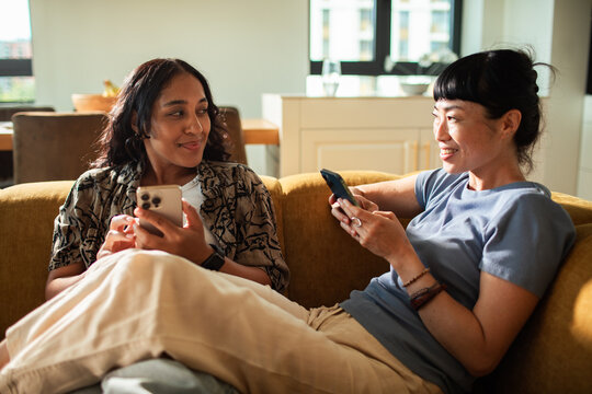 Two women using smartphones on sofa at home