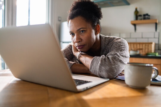 Focused woman working on laptop at home kitchen table