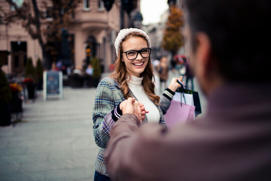Smiling young woman holding partner's hand while shopping on city street