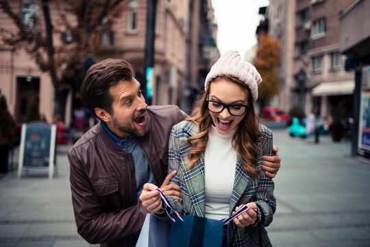 Happy couple opening shopping bag on city street