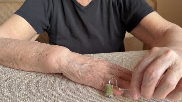 Elderly grandmother hand massage silver roller close detail of hands rolling sharp-edged metal roller across dry aged skin