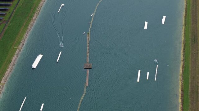 Aerial view of wakeboarding obstacles and ramps on a lake with solar panels on the shore and a person wakeboarding at Fenland Aqua Park in Whittlesey, England, United Kingdom.