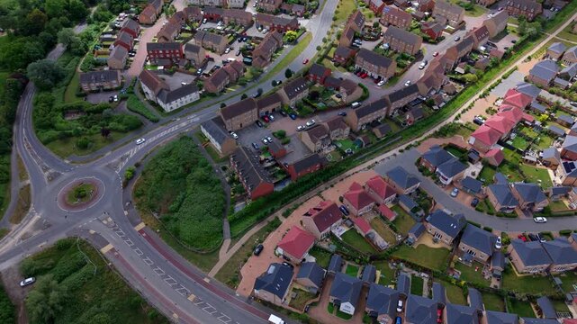 Aerial view of a modern residential neighborhood with suburban houses, a roundabout, and green gardens in Ely, England, United Kingdom.