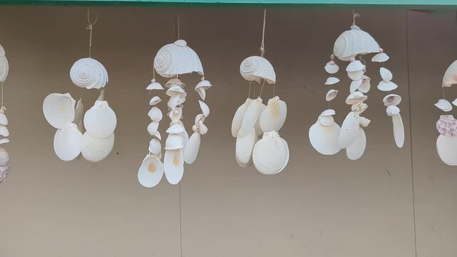 White shell wind chimes hanging outside a house wall. Handmade decor, coastal craft, home ornament, seaside souvenir, relaxing design.
