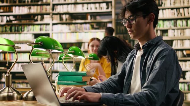 Asian student with glasses working on laptop at university library table, reading and typing information on computer during self study session, Focused academic environment, with academic research.