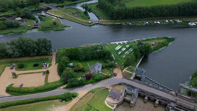 Aerial view of Denver Sluice complex with river gates, moored boats, and lush green banks at the junction of the River Great Ouse in Downham Market, England, United Kingdom.