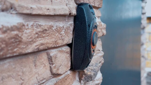 Middle of clip shows closeup of black intercom button fixed to rough beige brick wall on left foreground of frame, slightly wet with condensation and droplets suggesting recent exposure to