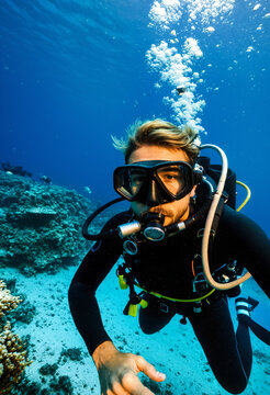 young adult male scuba diver taking a close up self portrait while exploring the underwater ocean environment with a vibrant coral reef and clear blue water.