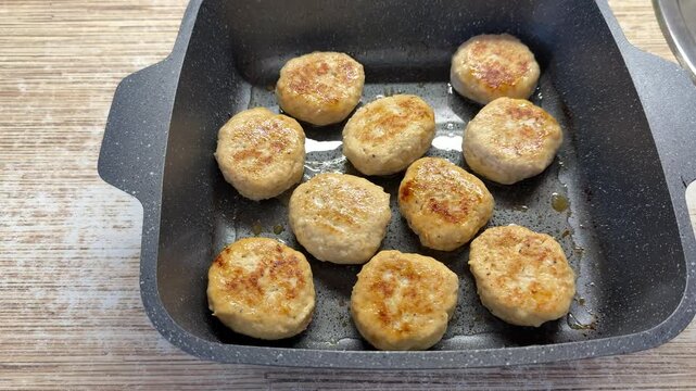 Close-up view of homemade beef and pork cutlets cooked in oil on rectangular baking sheet, with browned round patties resting on countertop during home kitchen meal preparation
