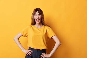 Obraz premium Confident woman in a yellow tee poses in a bright studio against a sunny yellow wall, showing a joyful, excited expression for a bold fashion and lifestyle portrait today