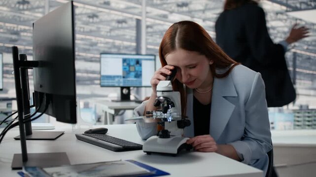 Woman in microelectronics development facility studying microchip architecture with microscope, female engineer using microscopy tool to research semiconductor materials in office.