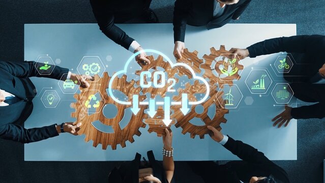A diverse business team collaborates around a table, using gears and digital elements to symbolize commitment to sustainability and reduction of carbon emissions in a modern office. Raster