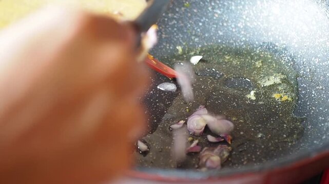 Cooking sliced shallots in hot oil in a pan with a spatula, close-up shot, preparation for Asian cuisine