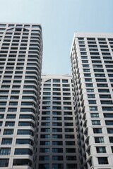 Fototapeta premium Three tall modern apartment buildings with many windows seen from below against a pale sky. Buildings have repetitive geometric facade patterns and light colored concrete material.