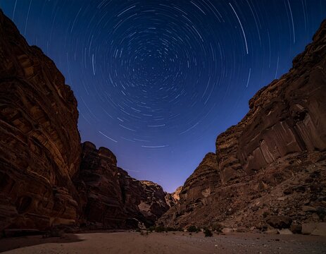 Night landscape looking down the multi-layered canyons of Khuren Khaniin Khets in Mongolia. Concentric circular star trails rotate over sharp geological strata. Cinematic 8k photo.