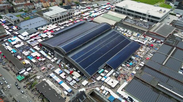 Aerial view of the Abattoir market with its solar-paneled roof and numerous colorful outdoor stalls and crowds of people in Anderlecht, Brussels, Belgium.