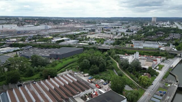 Aerial view of an industrial canal with locks, warehouses, and a cooling tower under a cloudy sky in Anderlecht, Brussels, Belgium.