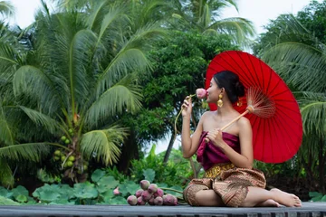 Fotobehang Lotusbloem Serene woman enjoys tropical escape holding vibrant red parasol amidst swaying palm trees and blossoming lotus flowers  wearing traditional patterned clothing and golden earrings, creating peaceful mo  © AU USAnakul
