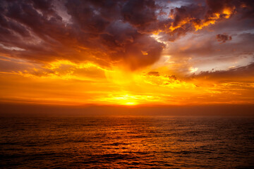 Fototapeta premium Golden sunrise over the ocean with dramatic clouds and glowing reflections on the water surface along the Sydney coastline, Australia.