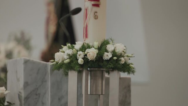 White roses and greenery decorate marble altar with paschal candle in church